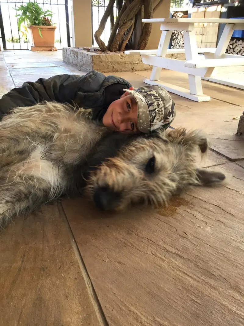 Boy lying on a tiled patio cuddling a relaxed Irish Wolfhound