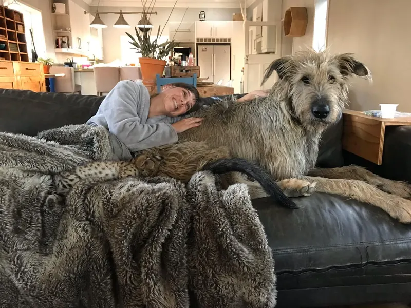 Woman relaxing on a couch beside a large wheaten Irish Wolfhound